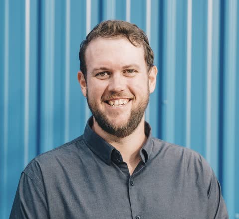 Robert Gilbert smiling, in a gray button-up shirt, in front of a blue corrugated metal wall.