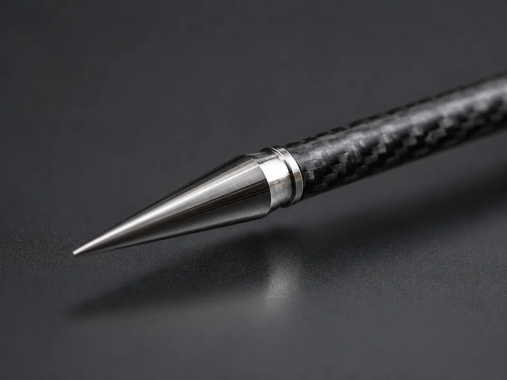 Close-up of a polished steel field point screwed onto the front of a carbon-fibre arrow shaft on a dark studio background.